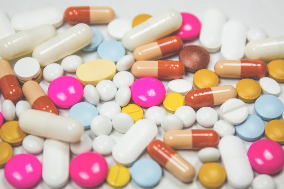 A mix of colorful pills and capsules scattered on a white surface, representing pharmaceuticals.