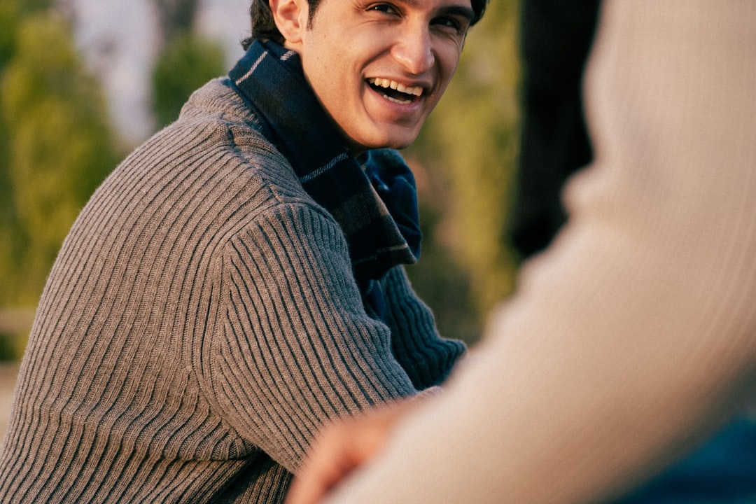 Man in a gray sweater laughing outdoors