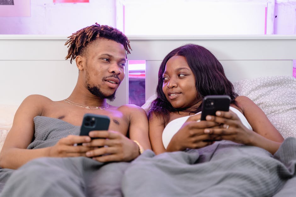A young couple enjoying each other's company while lounging in bed with their smartphones.