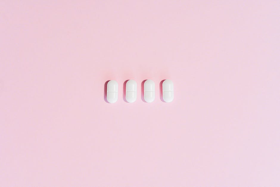 Four white capsules aligned on a soft pink background with empty copyspace.