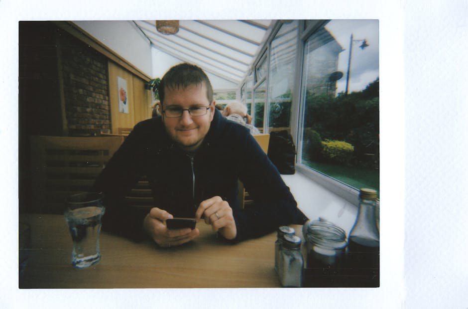 Man sitting with smartphone at a cozy restaurant table. Instant film captures candid dining moment.