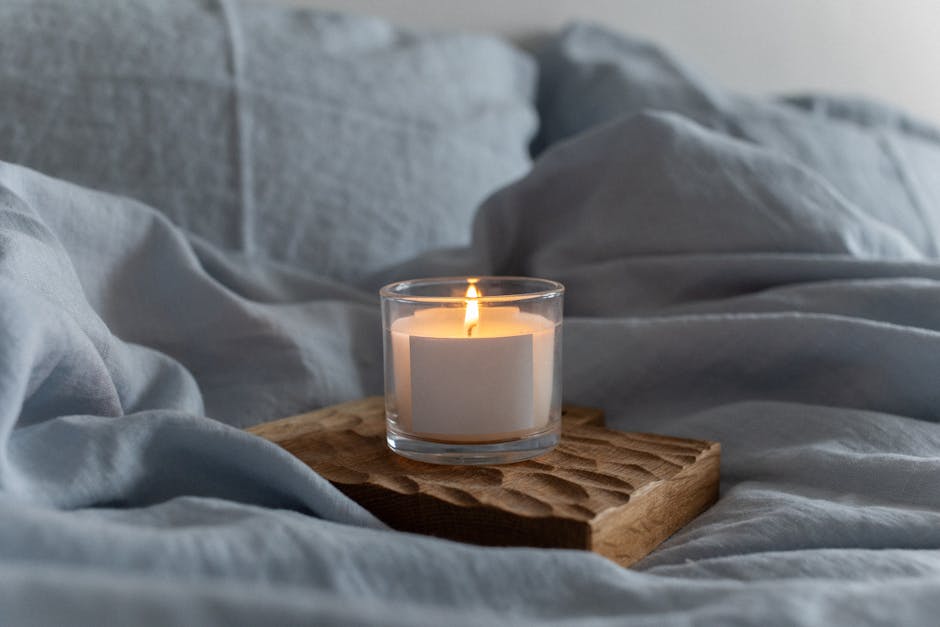 Close-up of a burning candle on a bed with soft linens, creating a warm and cozy atmosphere.