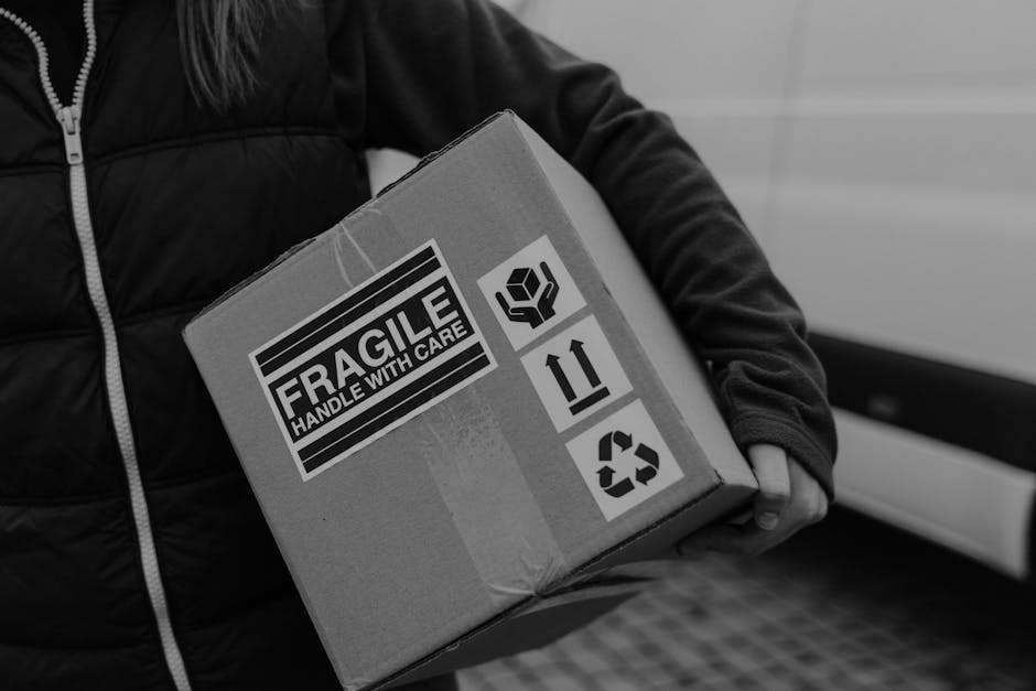 Black and white image of a courier carrying a fragile box with care labels.