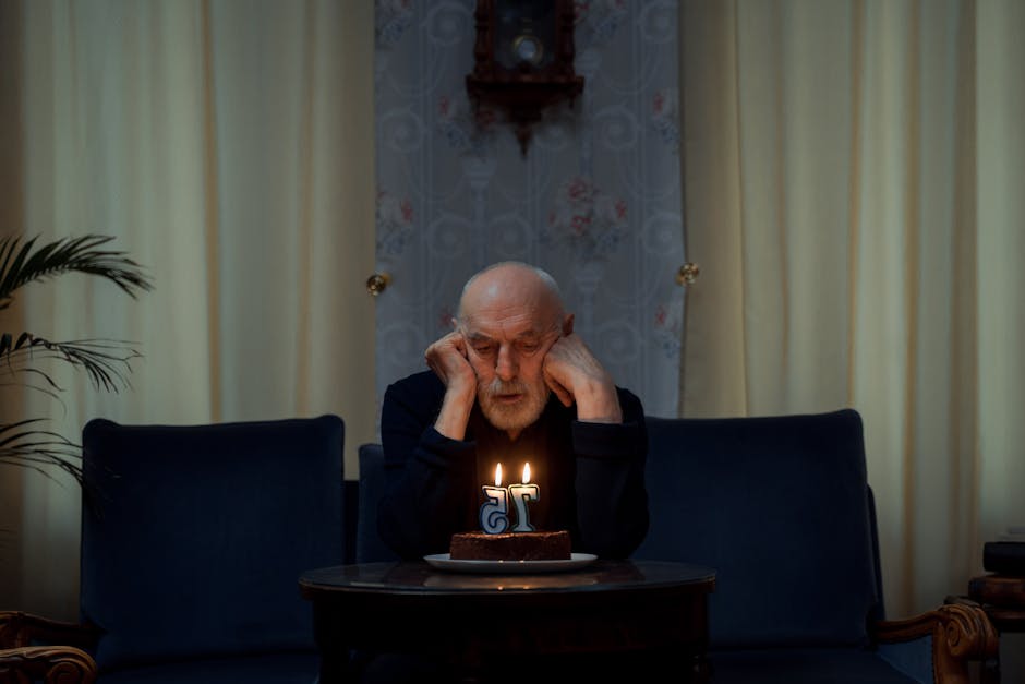 A senior man sitting thoughtfully by a lit birthday cake with a '75' candle indoors.