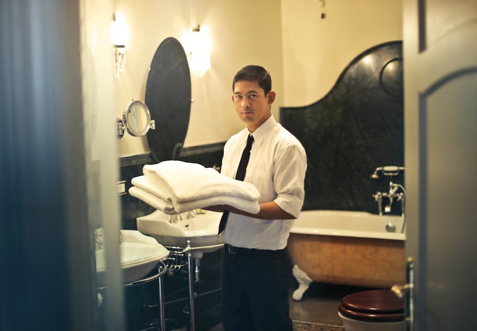 A hotel employee holding towels in a luxury bathroom with elegant decor.