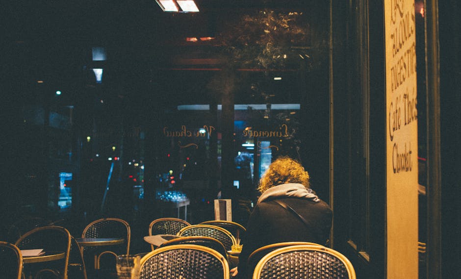 A solitary figure sitting in a warm, dimly lit Paris cafe during the evening.