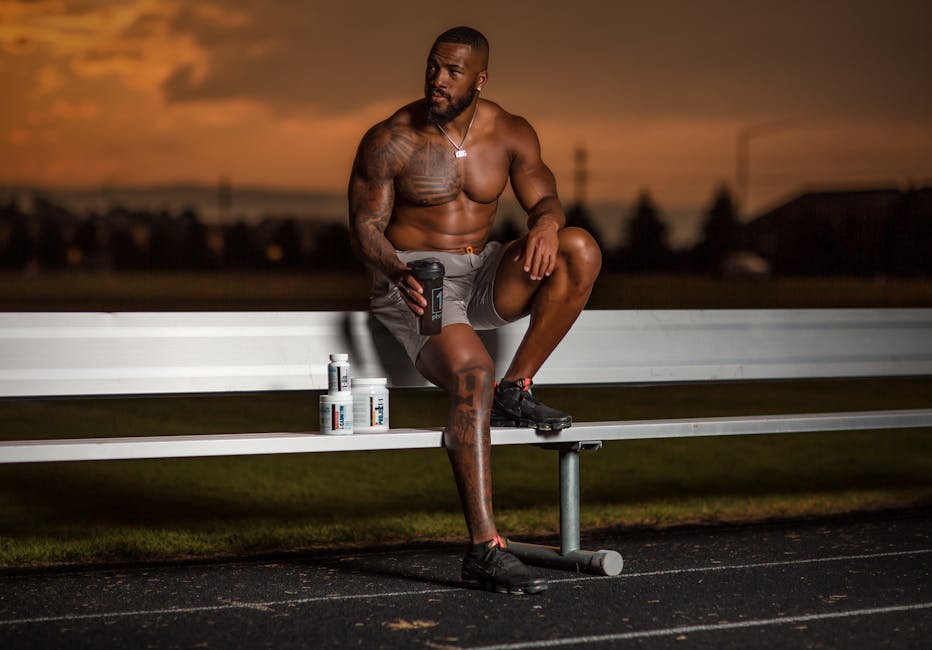 Muscular athlete sitting on a bench with supplements, enjoying a sunset at an outdoor stadium.