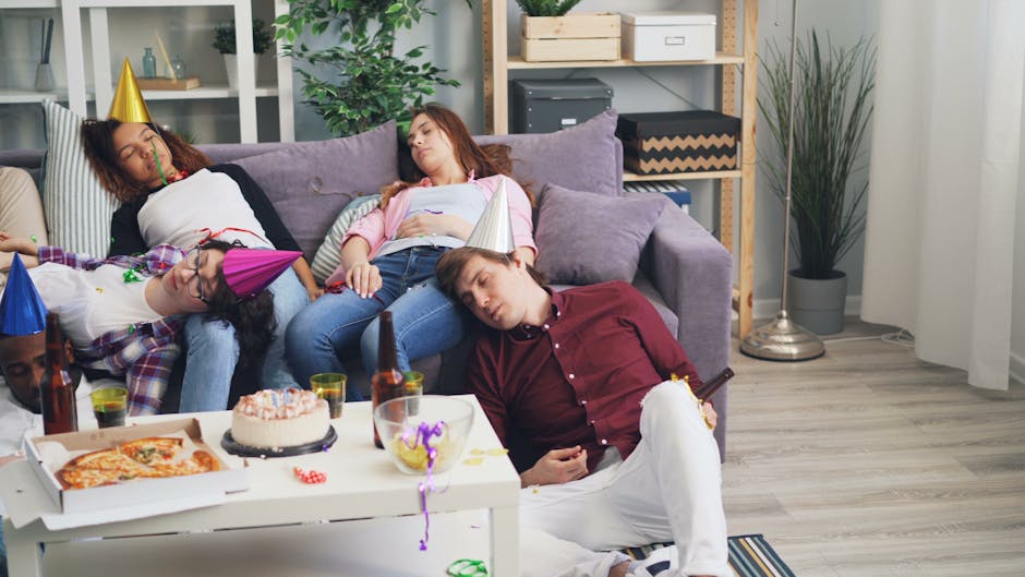 Group of friends asleep on a sofa after a lively party. Celebration remnants visible.