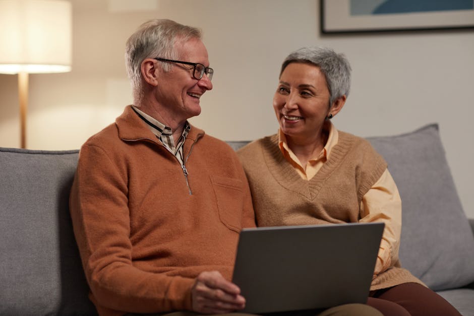 Senior couple smiling and using a laptop together in a cozy living room.